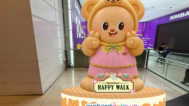 A large Butterbear figure in a pink dress and bear-ear hood standing inside orchardgateway on a base reading Butterbear HAPPY WALK