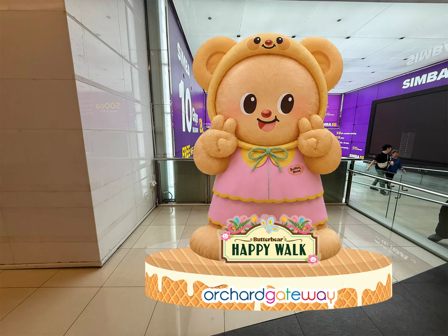 A large Butterbear figure in a pink dress and bear-ear hood standing inside orchardgateway on a base reading Butterbear HAPPY WALK