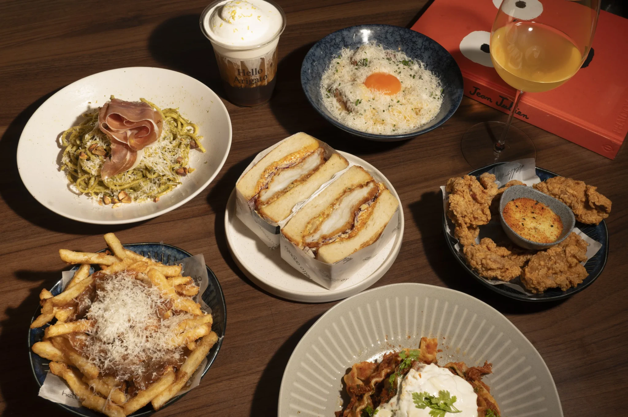 Overhead view of Hello Arigato dishes: pasta, sandwiches, fried chicken, fries, and plated entrée with drinks