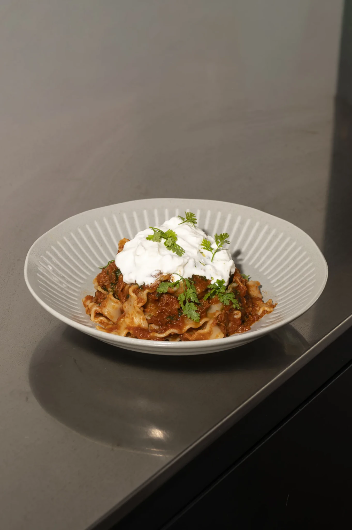 Kurobuta Ragu Pasta in a ribbed white bowl with a creamy white topping and green garnish