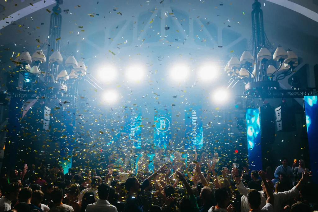 A party crowd under stage lights and falling confetti at an earlier Amber Lounge night.