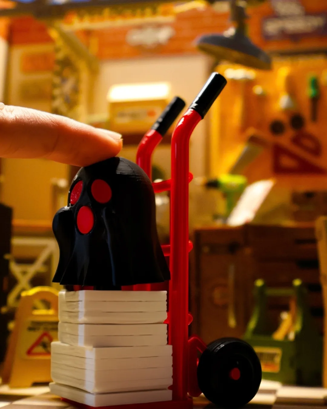 A black 3D-printed ghost figure with red details by Clik Clak, mounted on a red hand truck stacked with white blocks