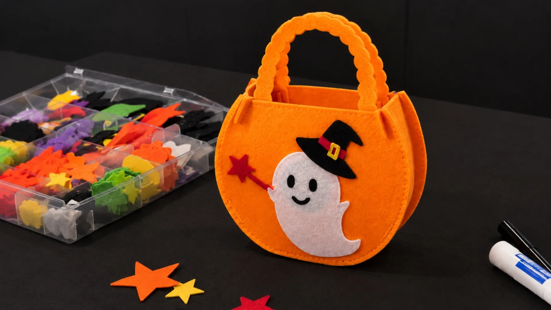 A workshop participant decorating an orange felt pumpkin bag with a ghost appliqué and a witch hat, with felt shapes and craft supplies alongside