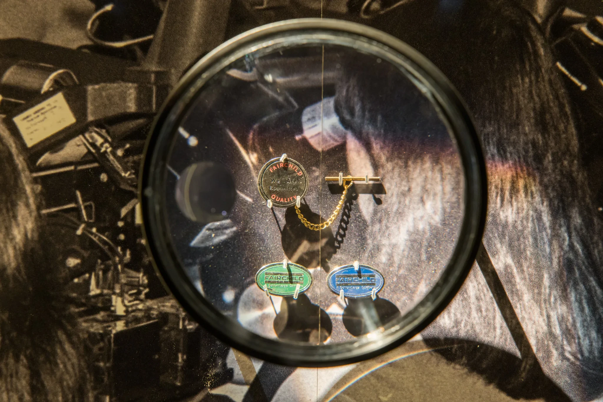 Fairchild Semiconductor collar pins, including a We Are Committed quality pin, seen through a magnifying lens
