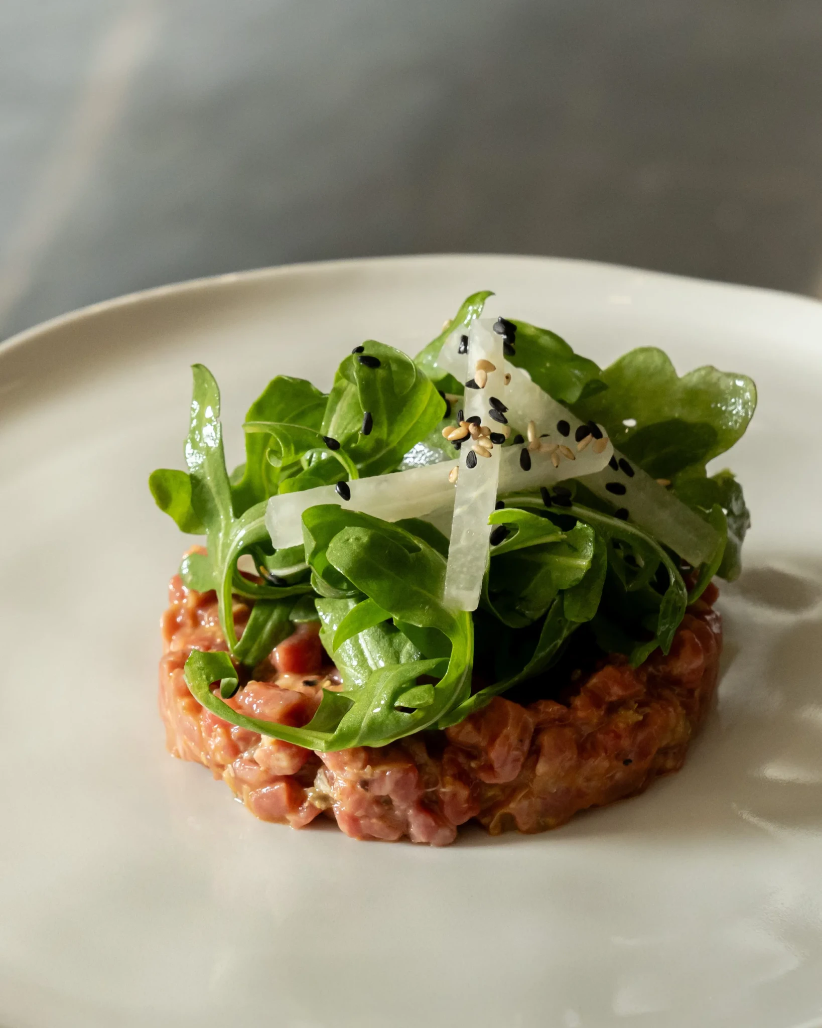 Tartare topped with rocket and shaved white radish with a sprinkle of black and white sesame