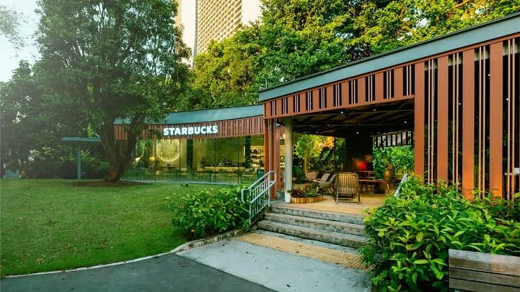 A Starbucks coffeehouse with wooden slat architecture and large glass windows, surrounded by lawn and greenery