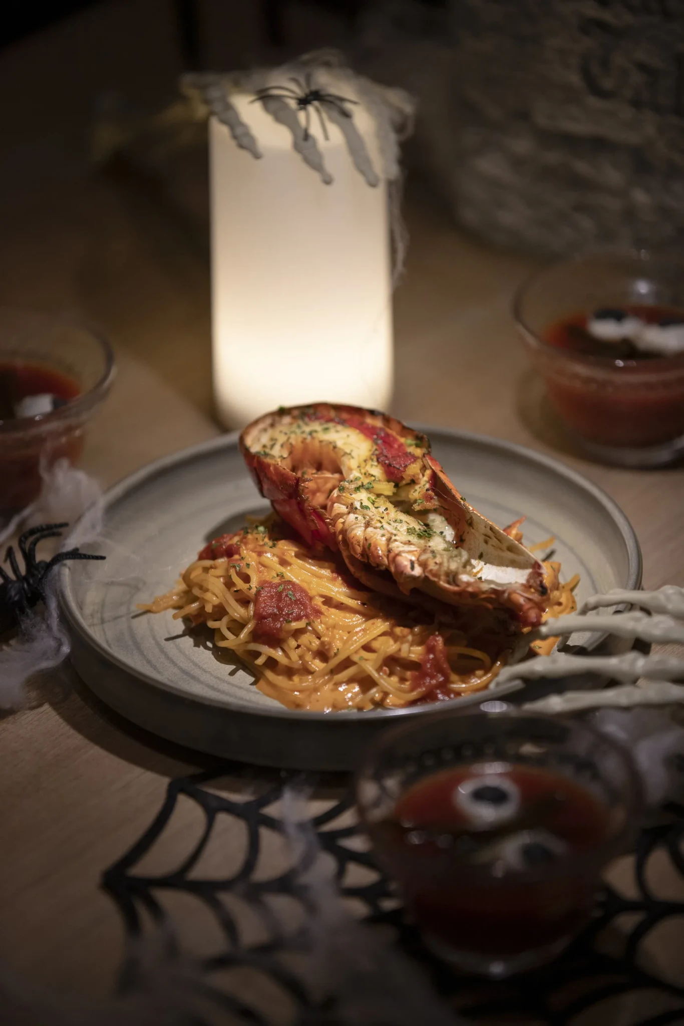 Grilled lobster half served over tomato-red spaghetti, styled with Halloween spiders and webbing