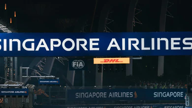The floodlit pit-straight gantry at the Marina Bay Street Circuit at night, with Singapore Airlines, FIA and DHL boards above the track and grandstands behind.