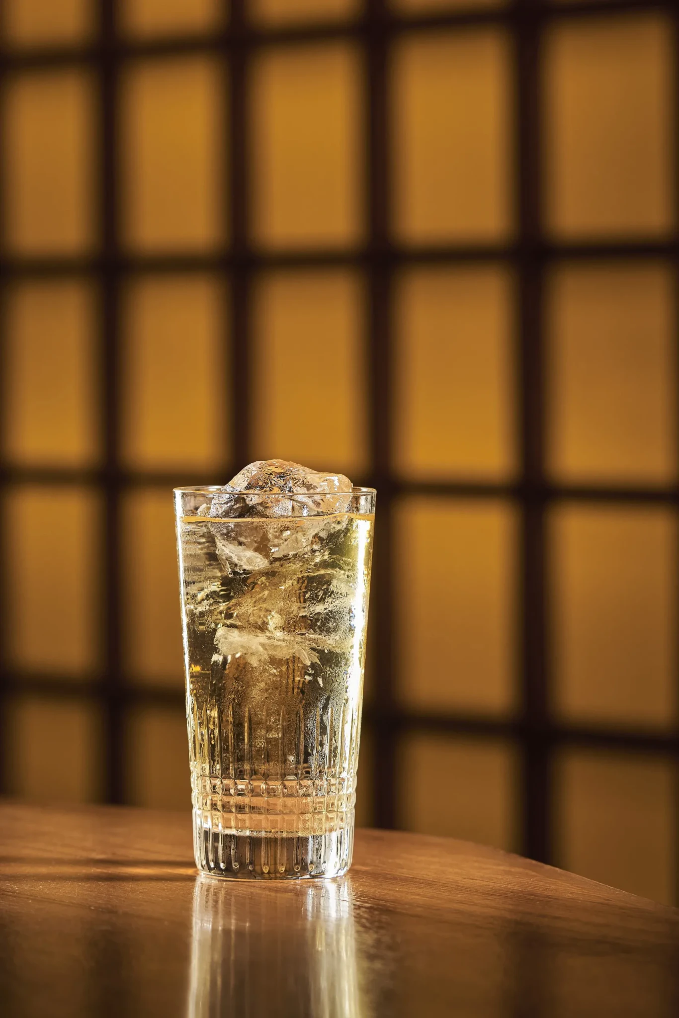 A Mizuwari whisky highball over a large ice cube in a ribbed glass on a wooden table