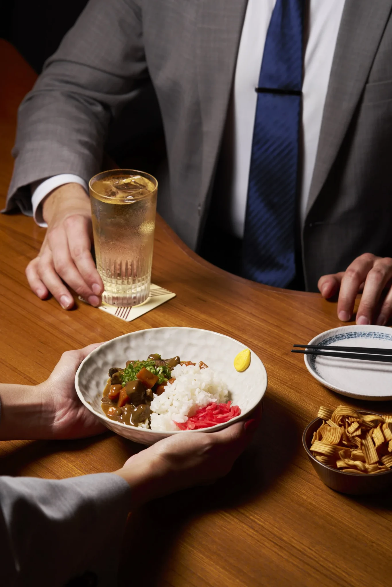 Gyutan Curry Rice in a white bowl with pickled ginger and mustard, beside a glass of amber drink over ice