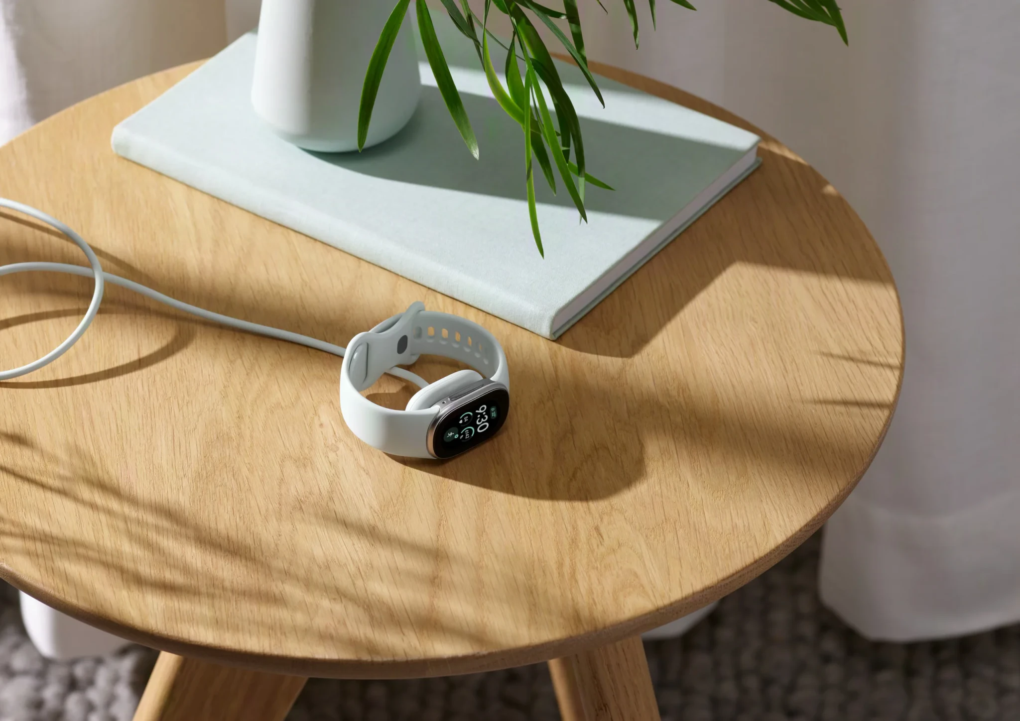 White Fitbit Edge tracker with charging cable lying on a round wooden side table