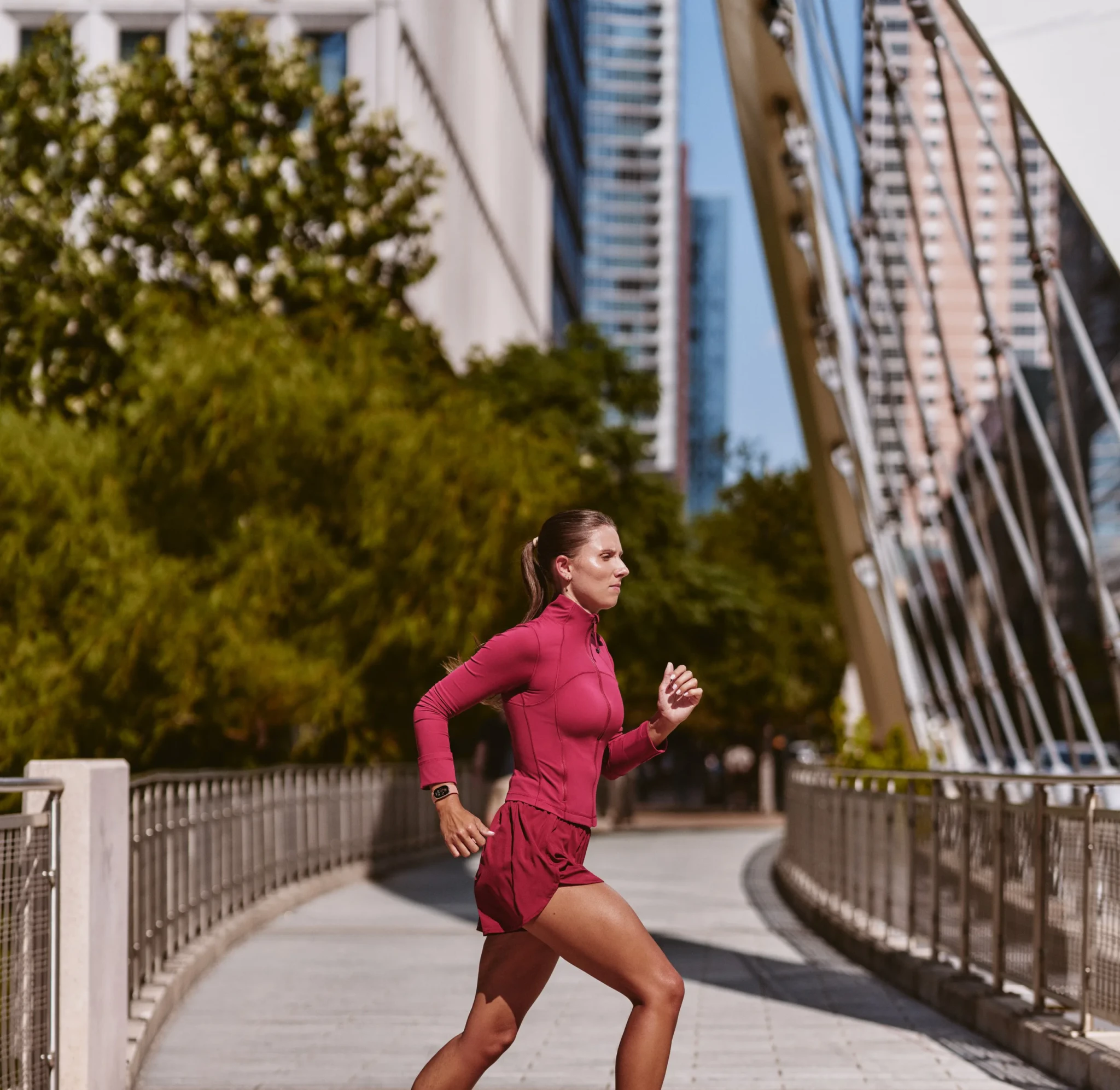 A woman runs across a city bridge wearing a Fitbit Edge on her left wrist