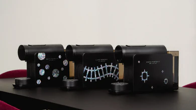Three black coffee machines with mother-of-pearl inlays of bubbles, a railroad track and stars on a dark table.