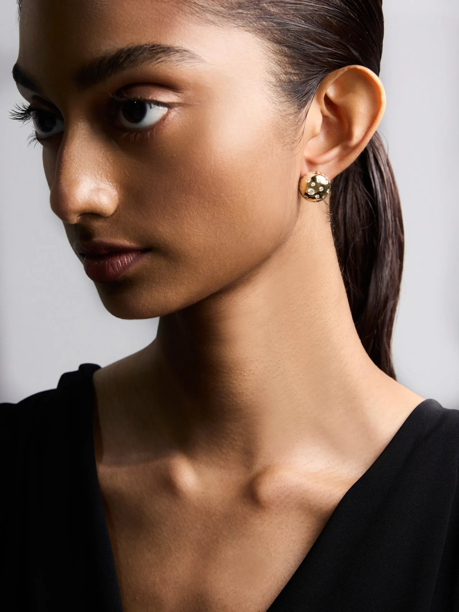A model wears the State Property Toadstool Diamond Earrings, polished gold dome studs set with white diamonds
