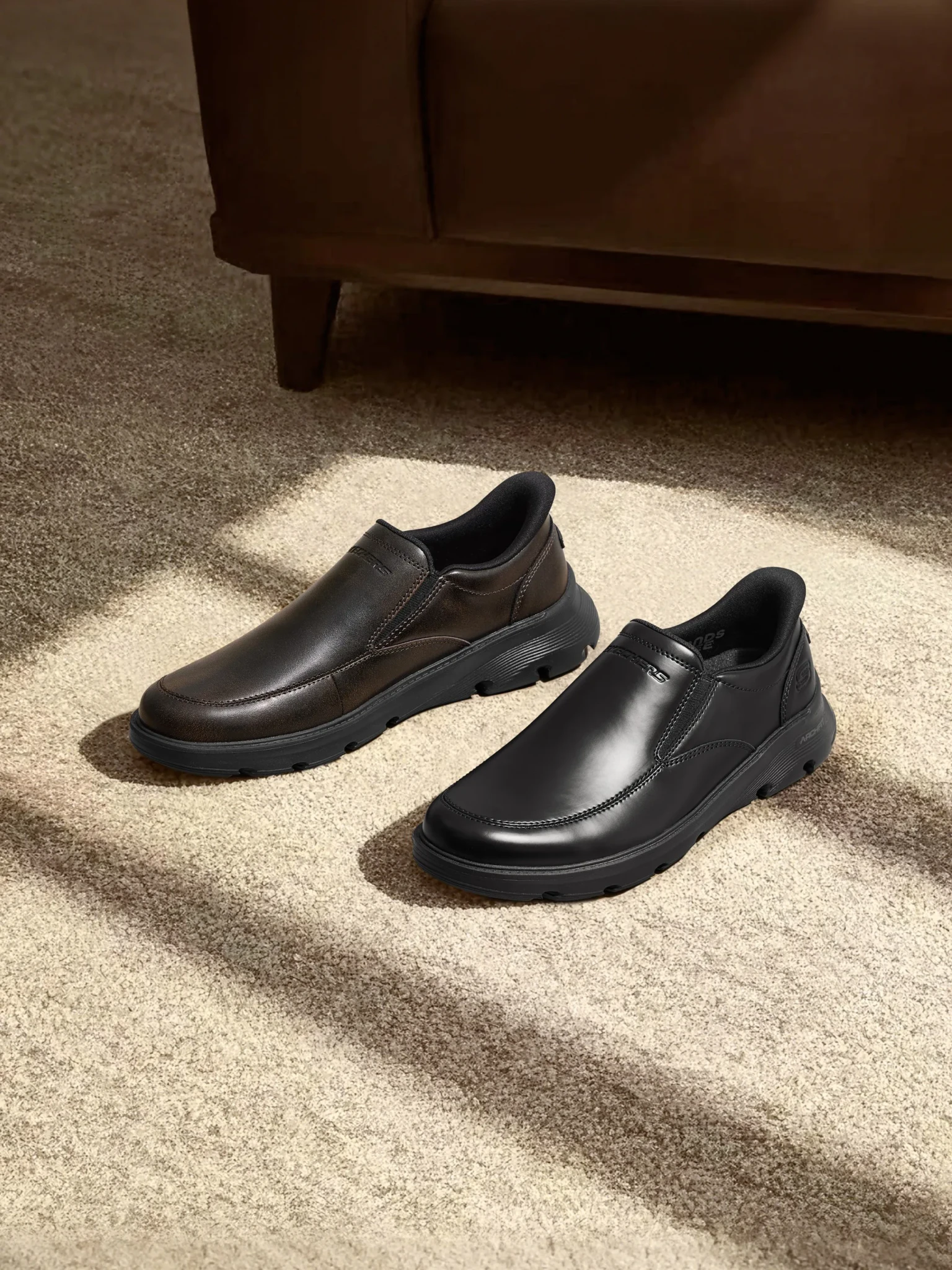 Brown and black slip-on shoes with thick rubber soles resting on a textured cream rug in soft light