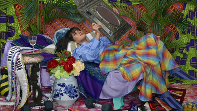 Wawi Navarroza's staged self-portrait showing a woman reclining beneath palm fronds holding an ornate mirror, with sashes printed ASIAN and ORIENTAL at her feet