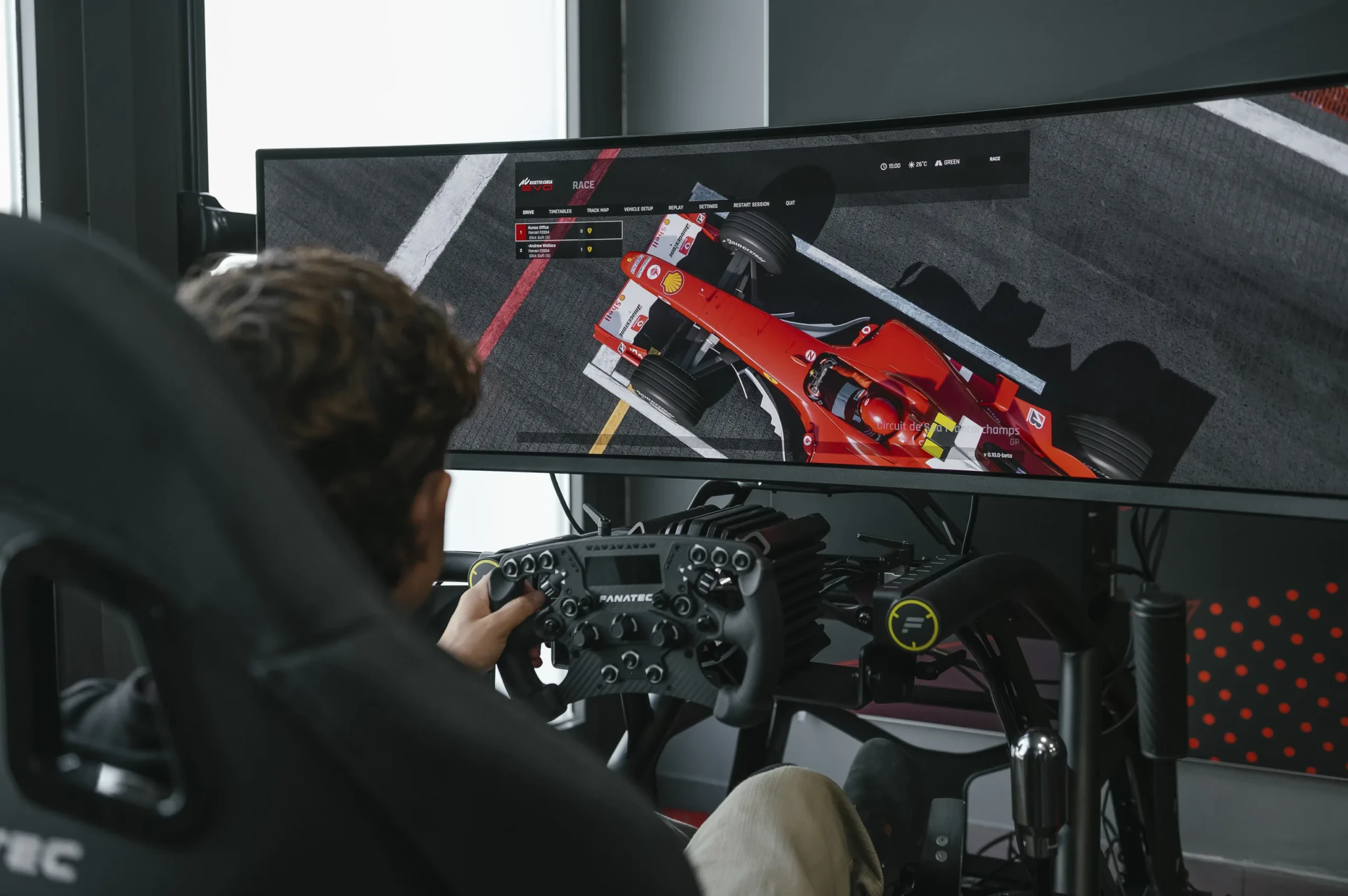 Gamer with Fanatec wheel controller playing Assetto Corsa EVO on ultrawide monitor, red Ferrari visible on screen