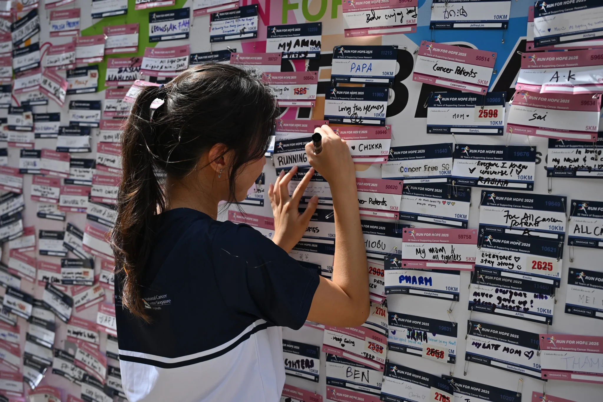A participant photographs a wall of race bibs with handwritten names and dedications