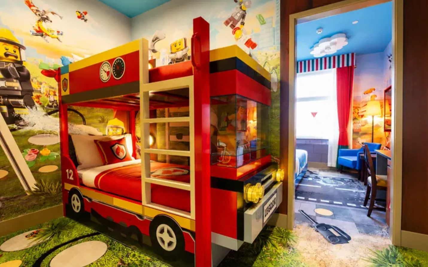 A red fire-truck bunk bed with LEGO minifigure murals on the walls