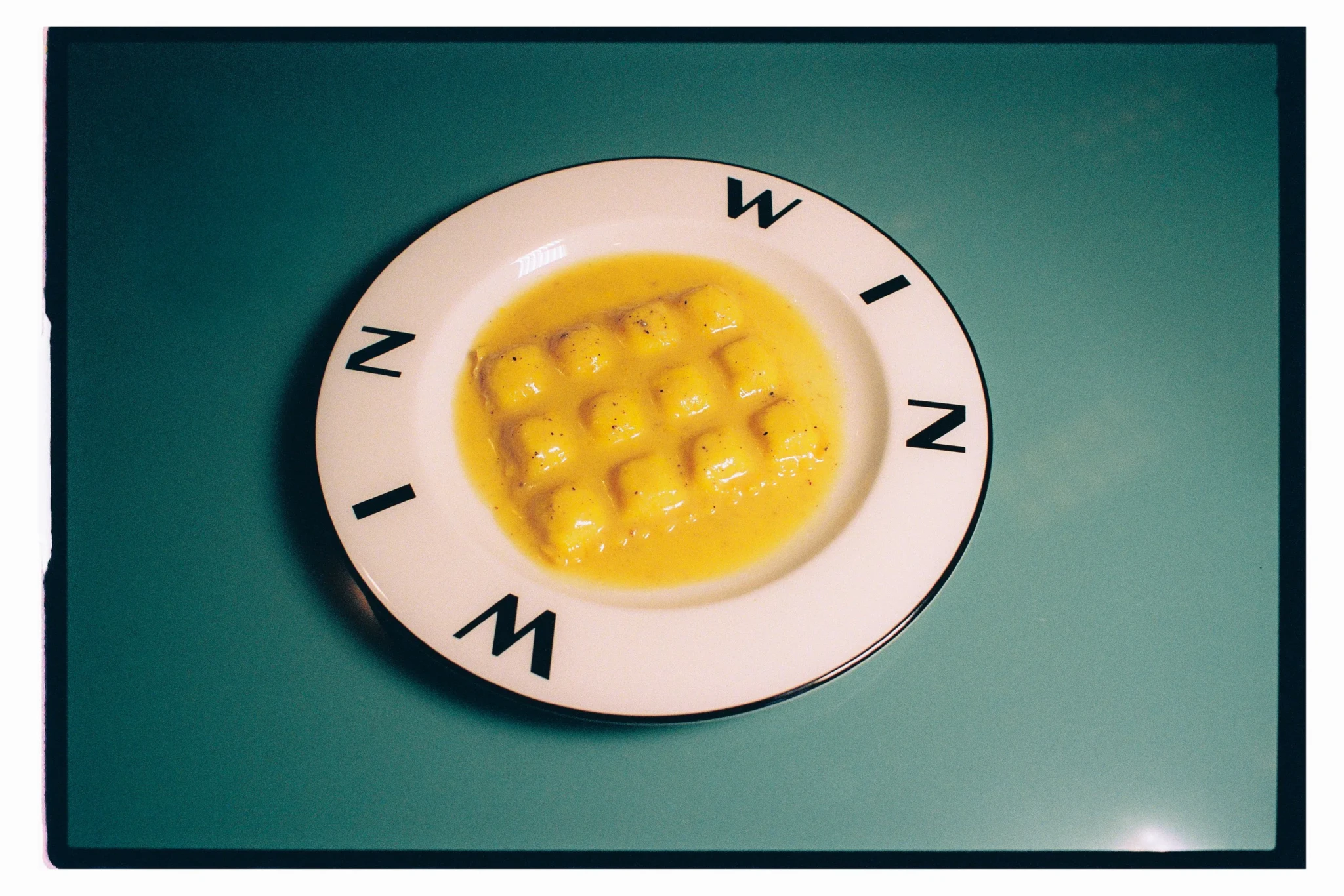Gnocchi in a golden sauce with cracked black pepper on a white plate rimmed with Win Win lettering