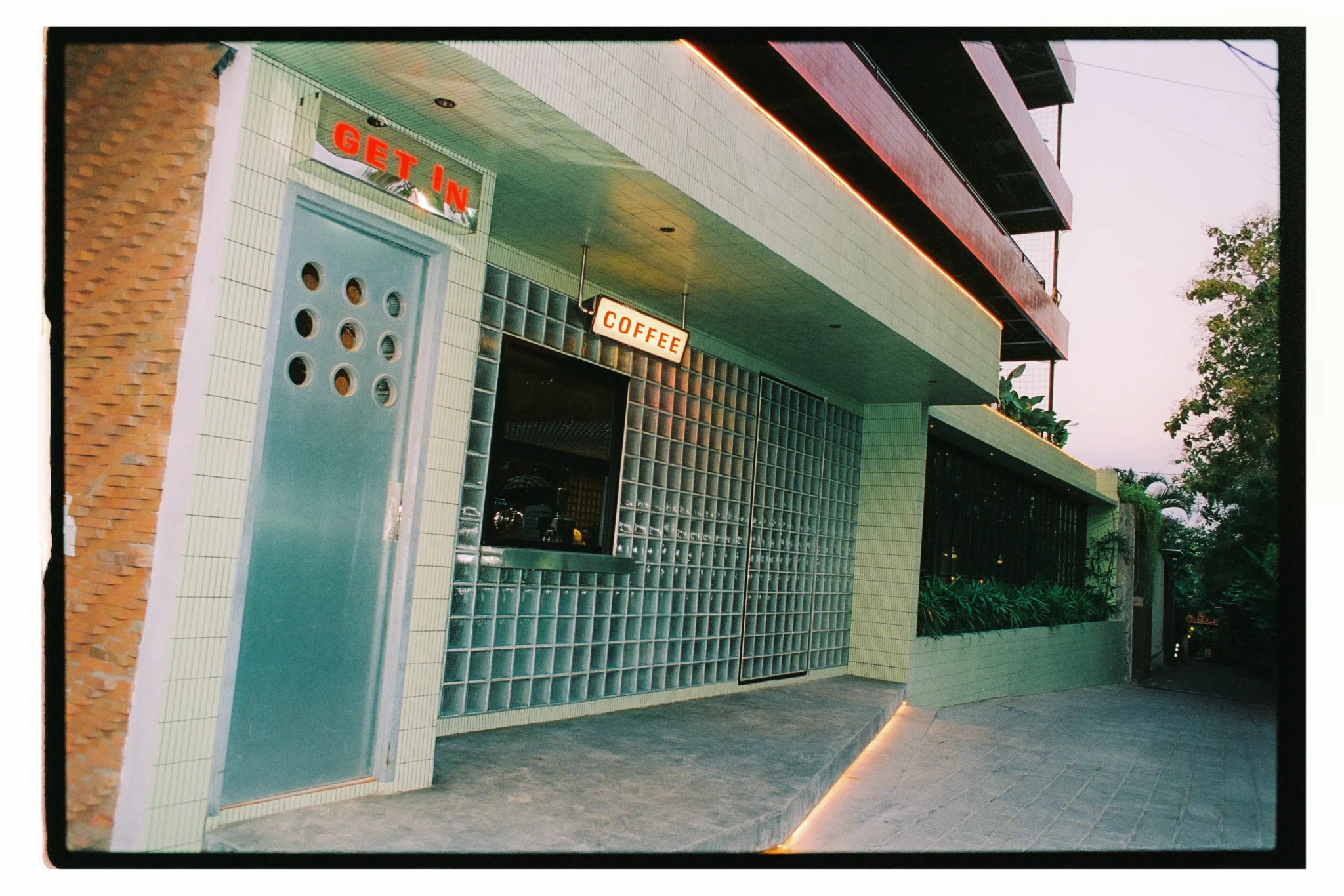 The street entrance of Etta The Place in Berawa, with a tiled facade, a glass-block wall and hand-painted 'Get In' and 'Coffee' signs