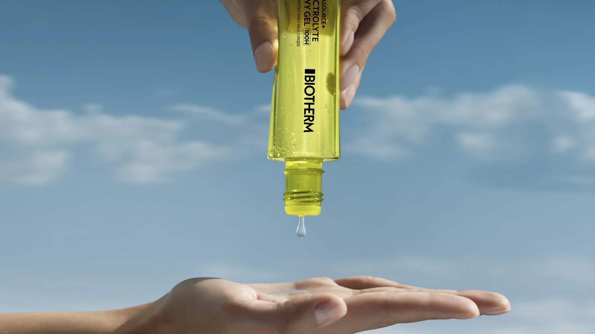Biotherm Aquasource+ Electrolyte Dewy Gel dripping from a yellow tube onto an open palm against a blue sky