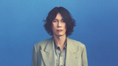 Kenshi Yonezu in a pale green suit against a blue backdrop