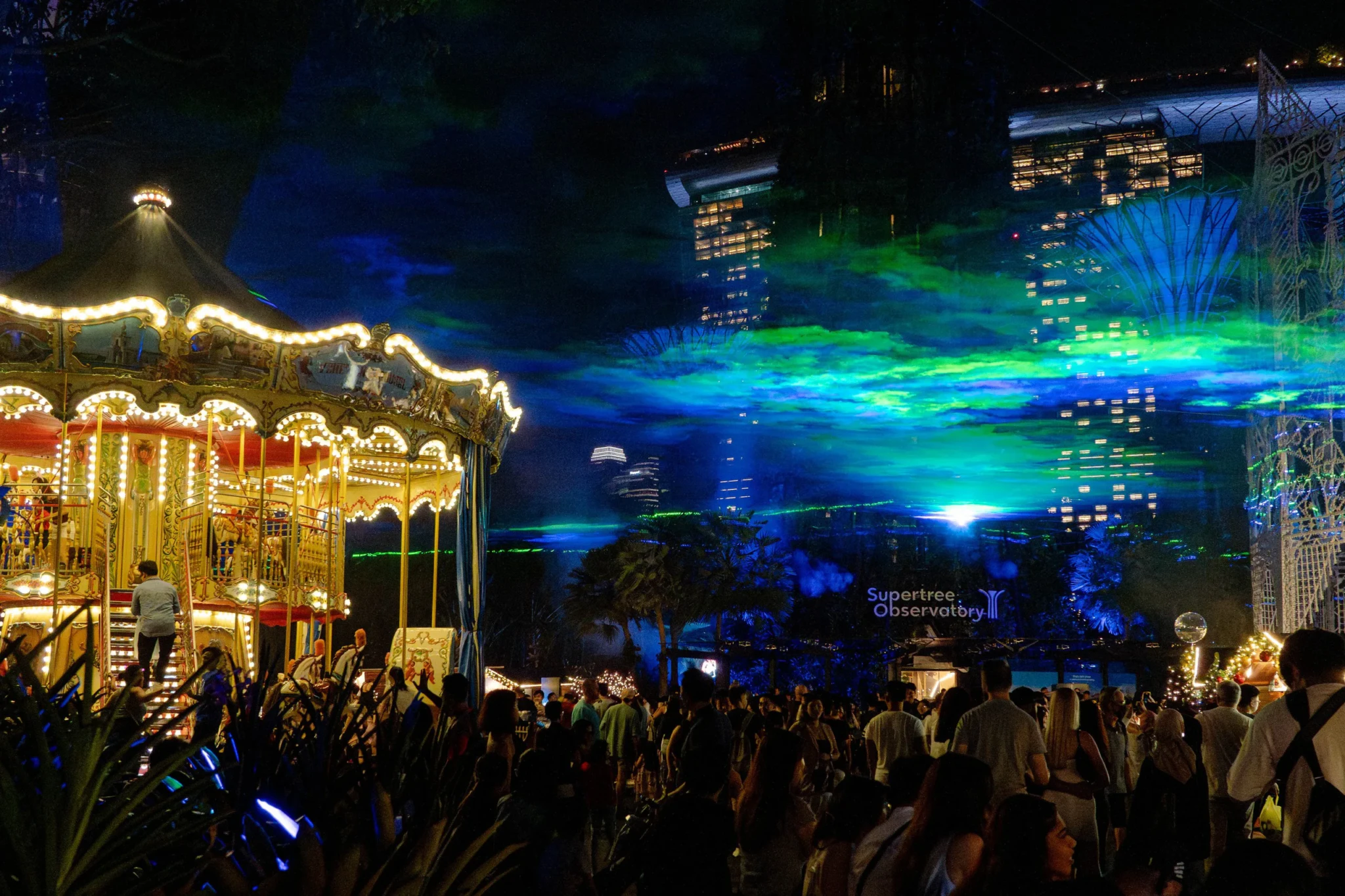 Green-and-blue lights above visitors and the carousel at Christmas Wonderland, Gardens by the Bay, in 2024