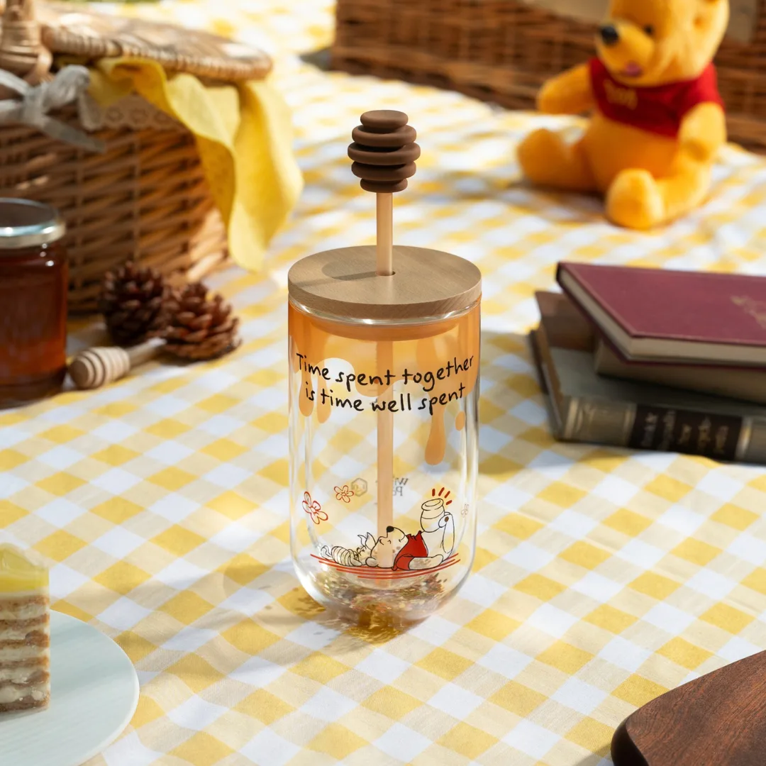 Glass tumbler with wooden lid and honey-dipper stirrer printed with Winnie the Pooh and the words 