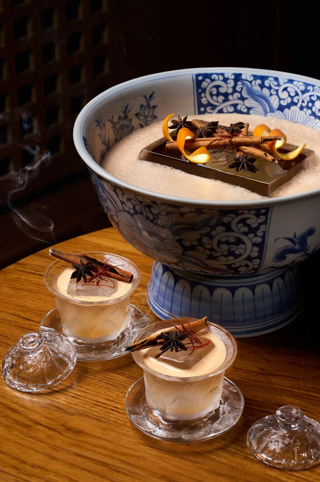 The Silk Road punch in a blue-and-white porcelain bowl topped with orange peel, cinnamon and star anise, with two iced glass cups