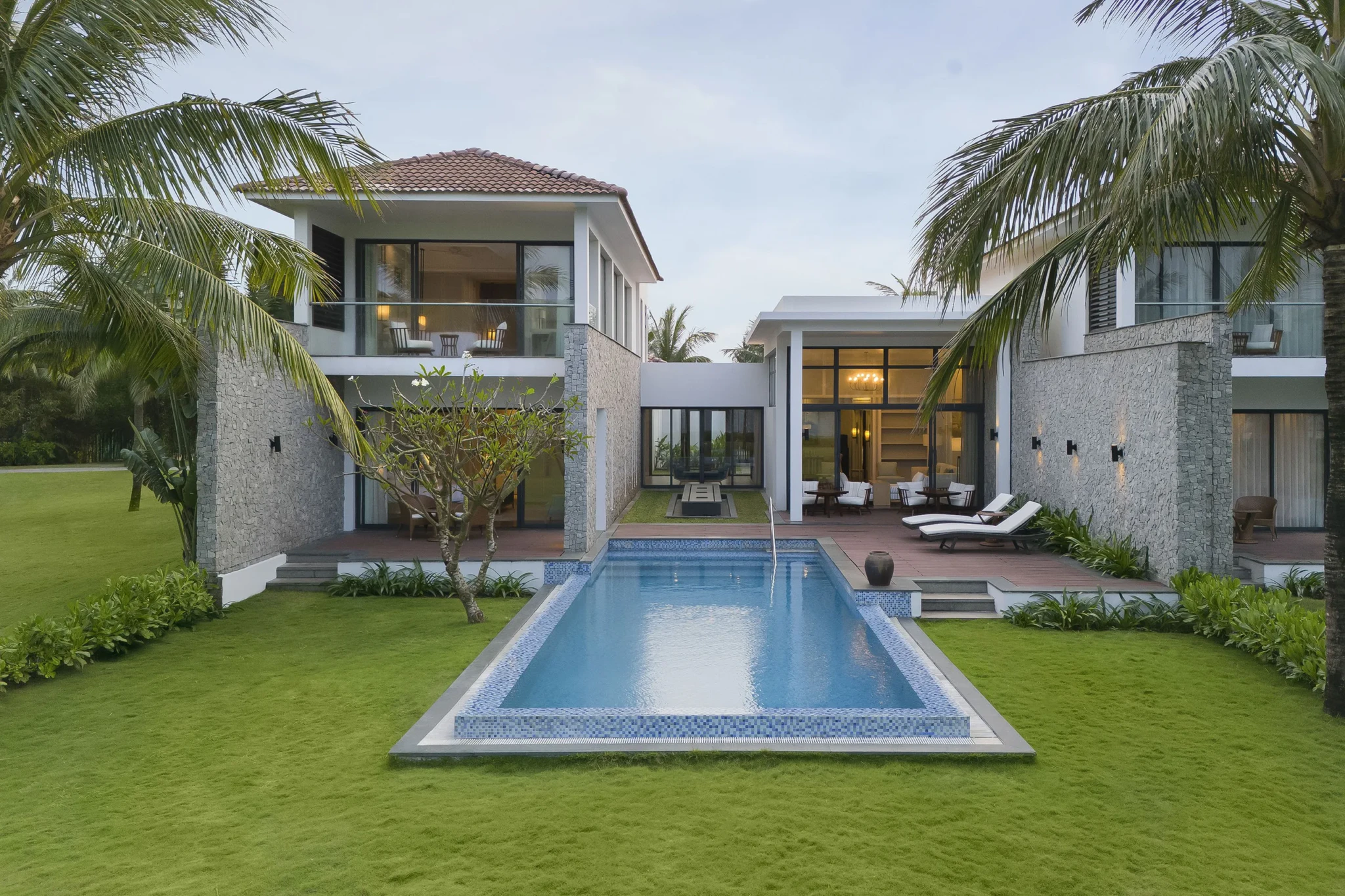 A two-storey stone-clad villa at Renaissance Danang Hoi An Resort & Spa with a rectangular pool, lawn and palm trees