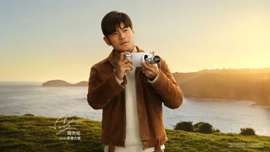 vivo brand ambassador Jay Chou holds a silver vivo phone fitted with a telephoto extender at sunset on a coastal cliff