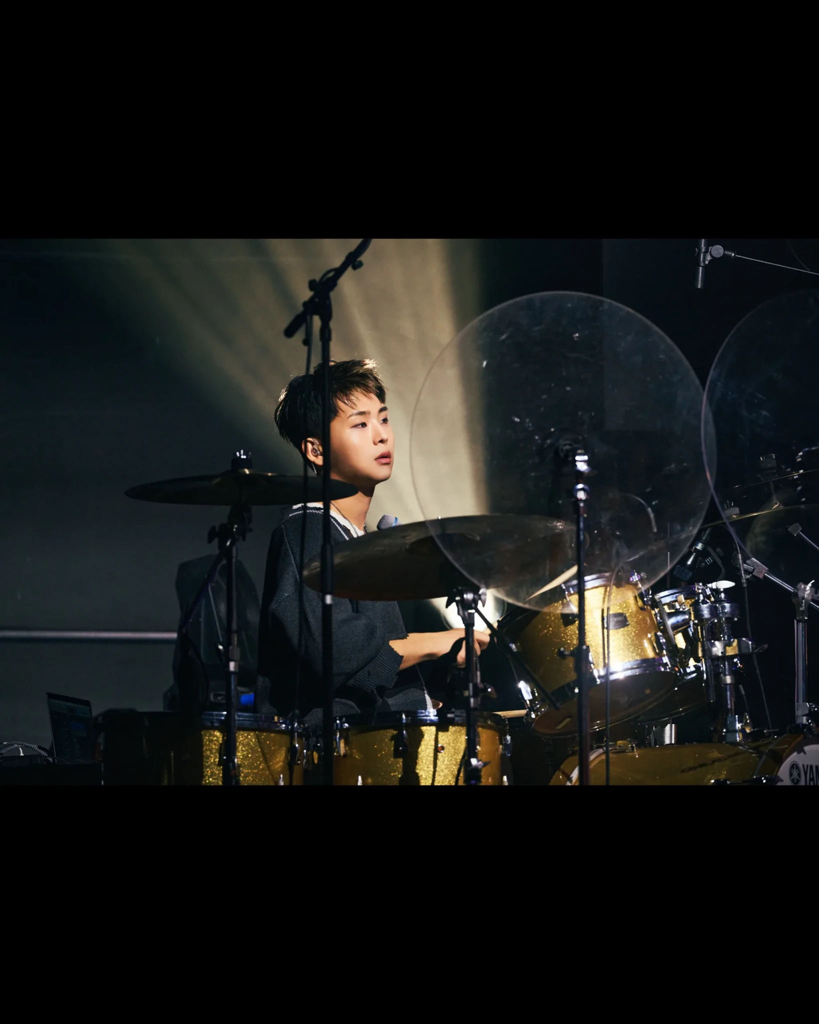 can't be blue's drummer playing a gold-sparkle Yamaha kit under a shaft of stage light behind clear acrylic shields