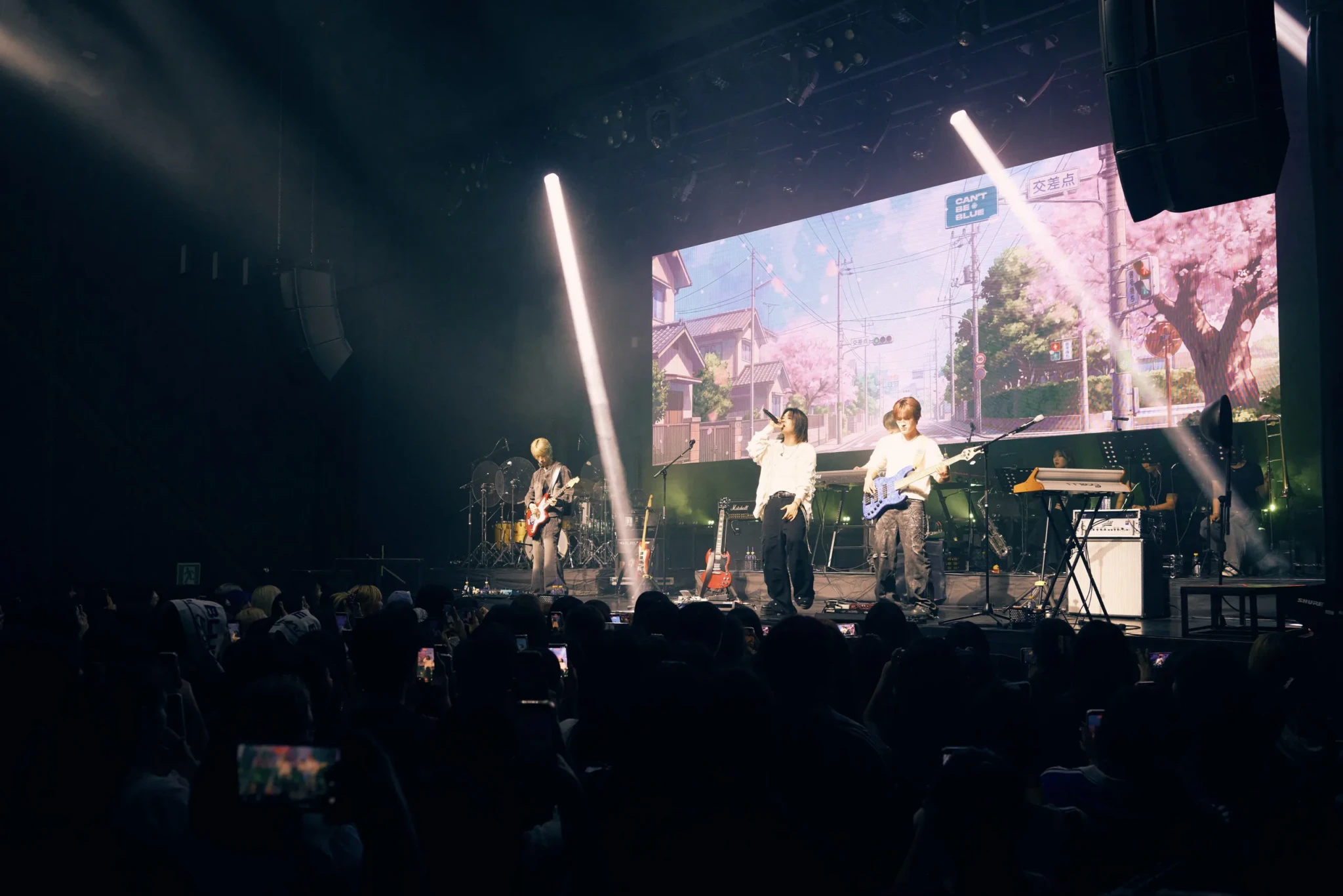 can't be blue performing on stage in front of a backdrop of a Japanese street lined with cherry blossom trees