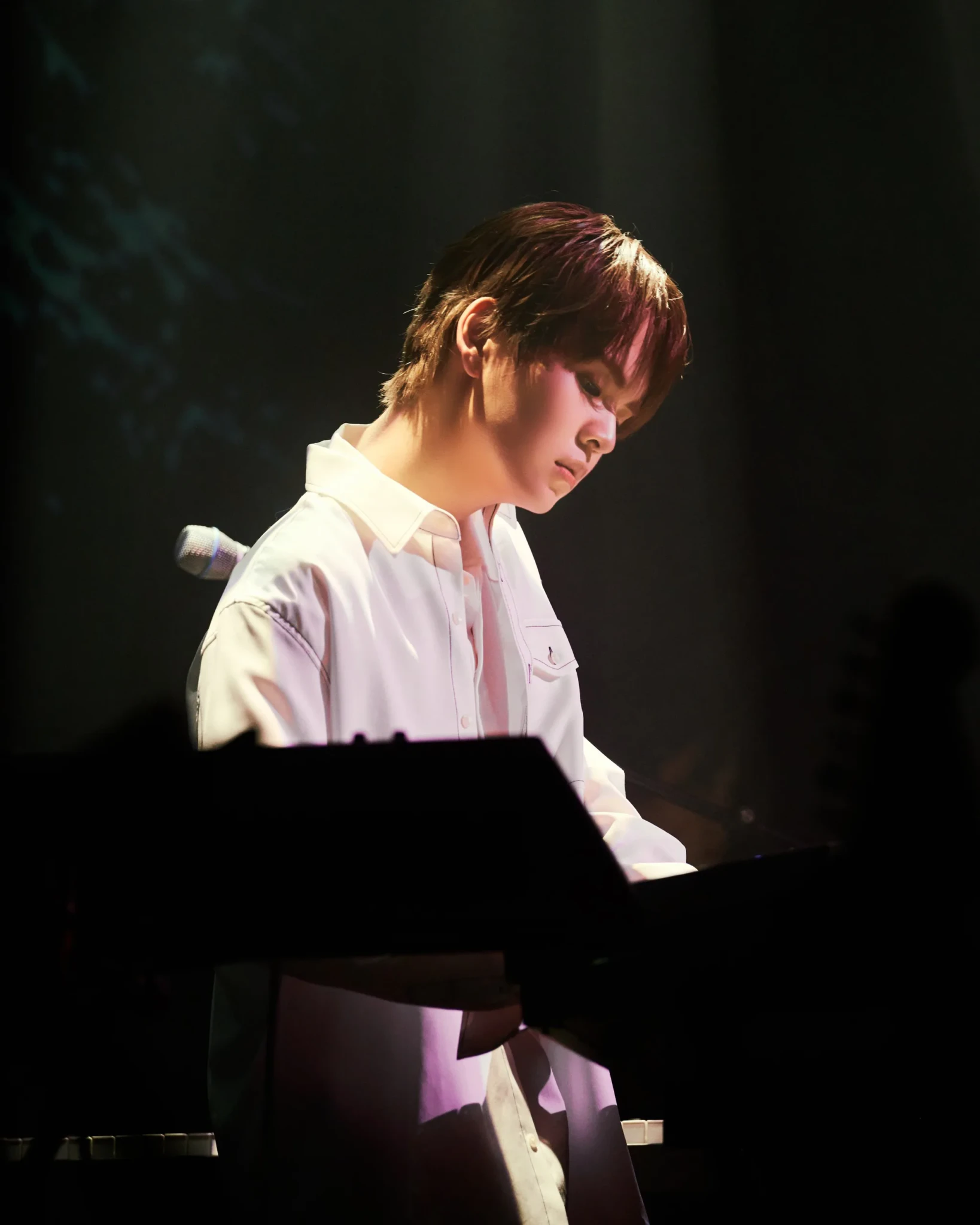 can't be blue's keyboardist in a white button-up shirt playing under a dark, moody spotlight