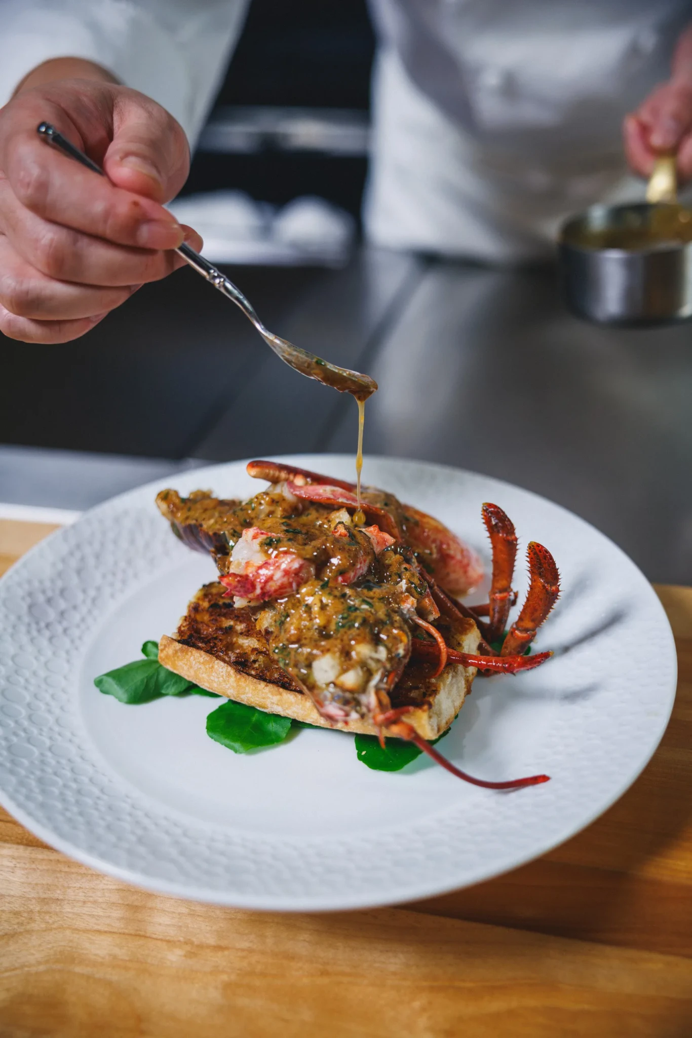 Braised Canadian lobster on grilled bread with a glossy herb sauce being spooned over it at Waku Ghin