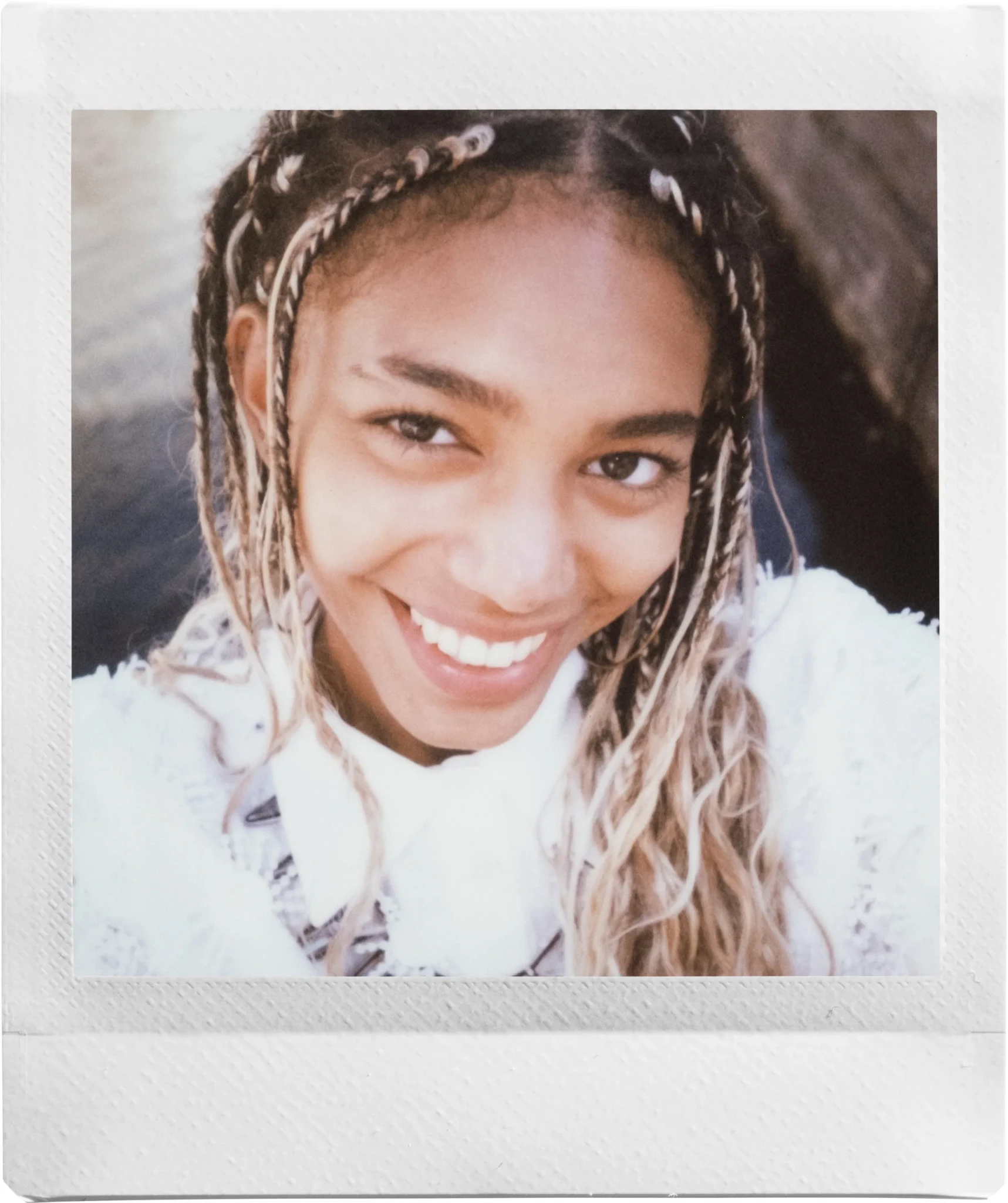 A smiling young woman with braided hair in white lace-trimmed clothing, photographed in square instant-film style