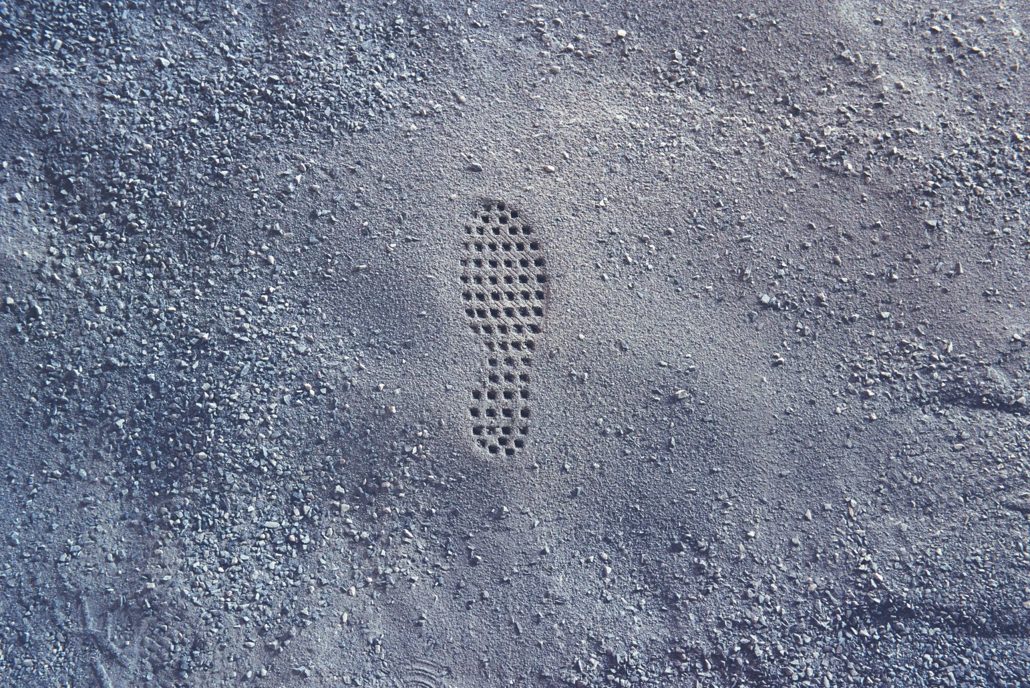 A circular shoe tread imprint pressed into a gravel-dusted grey surface