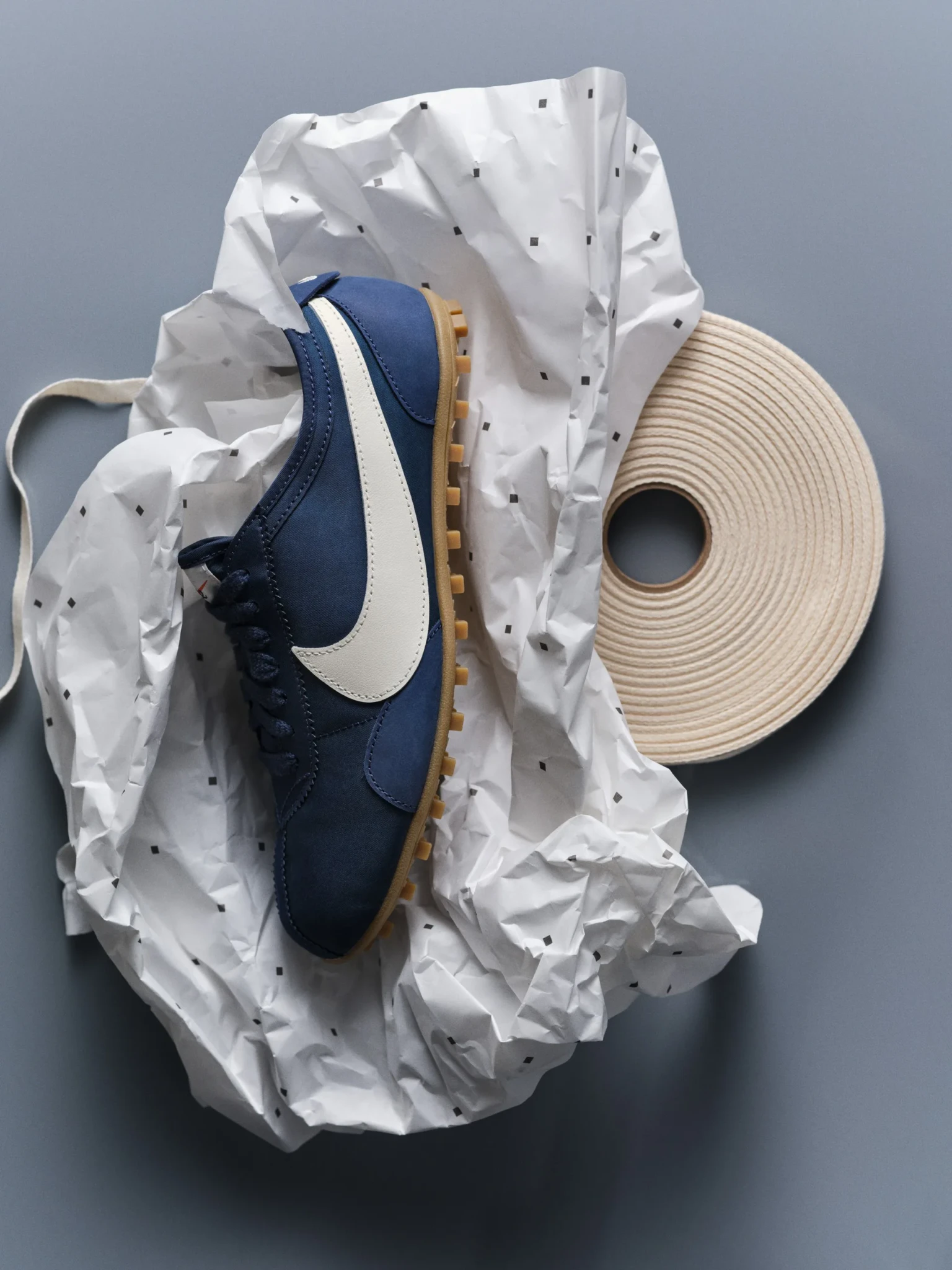 A navy and cream Nike Moon Shoe with a gum sole on printed white tissue paper beside cream ribbon