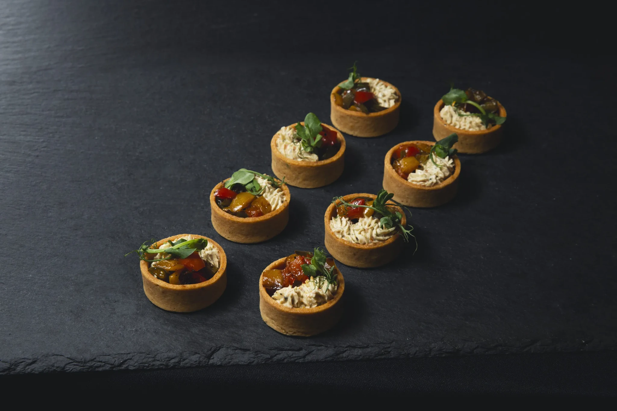 Roasted capsicum and cream cheese canapés in golden tart shells topped with microgreens on a slate board