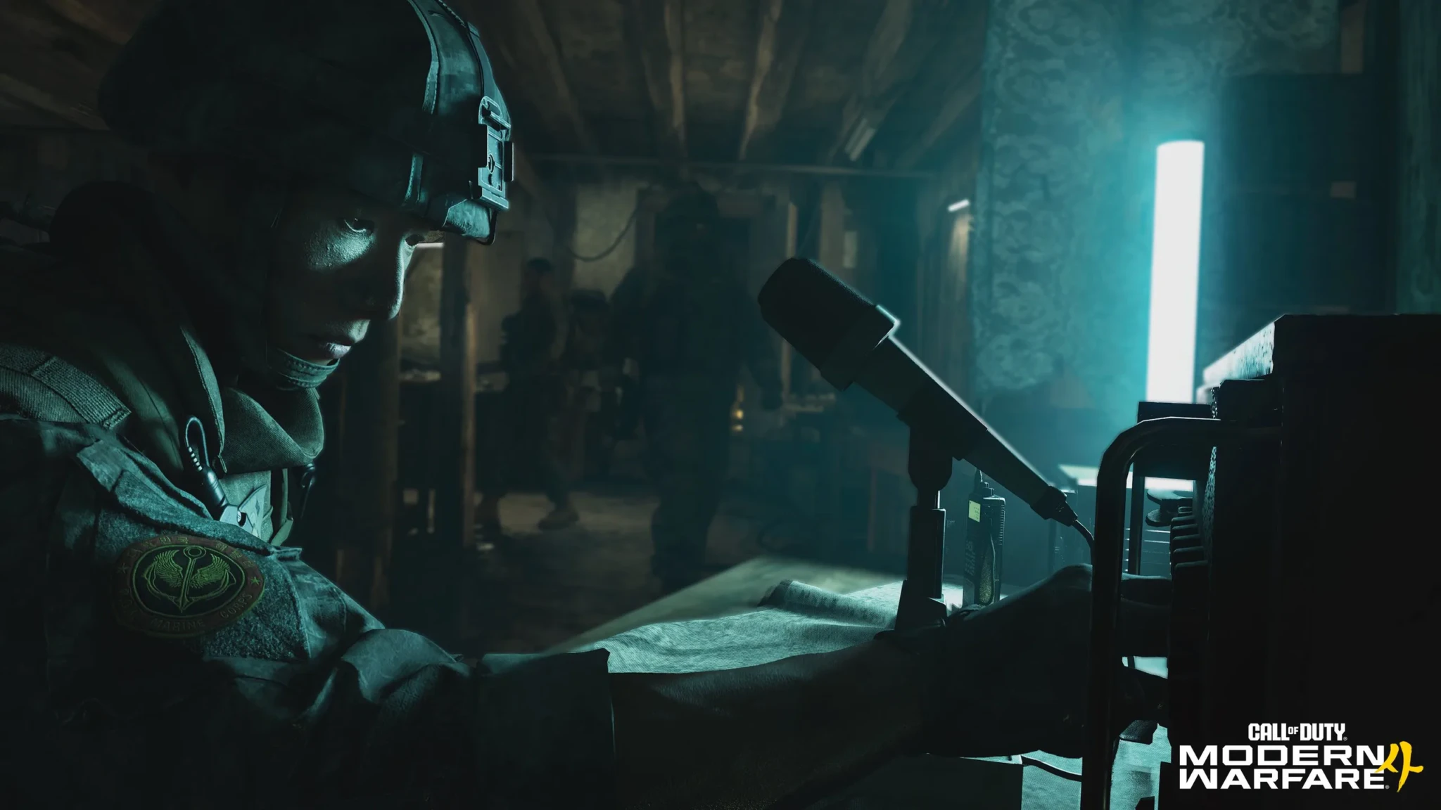 A soldier in a helmet and tactical gear sits at a desk beside a microphone in a dimly lit bunker in Call of Duty: Modern Warfare 4