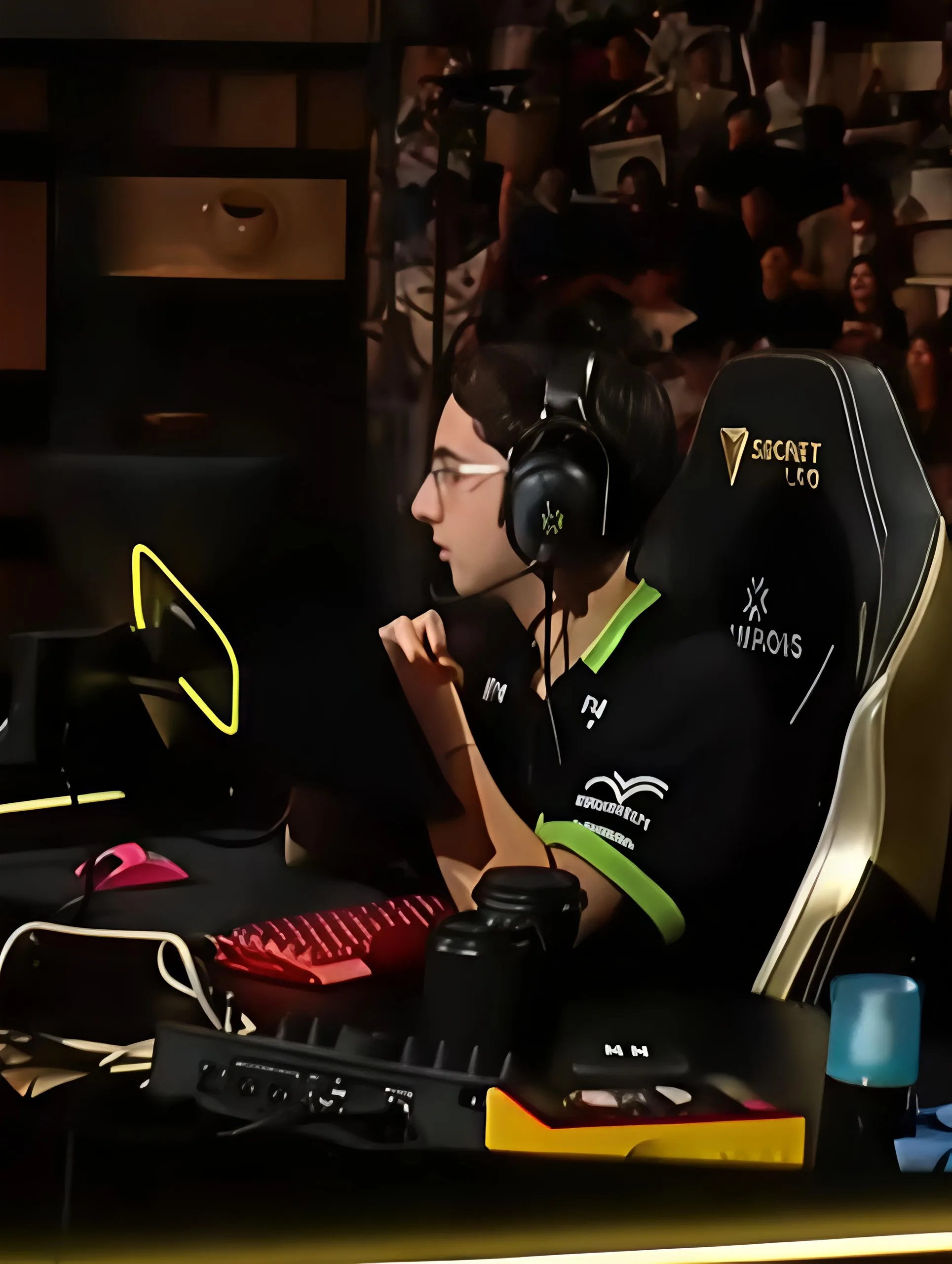 A LOUD player in a black jersey with green trim and headphones sits in a gaming chair at his desk, with the crowd visible behind