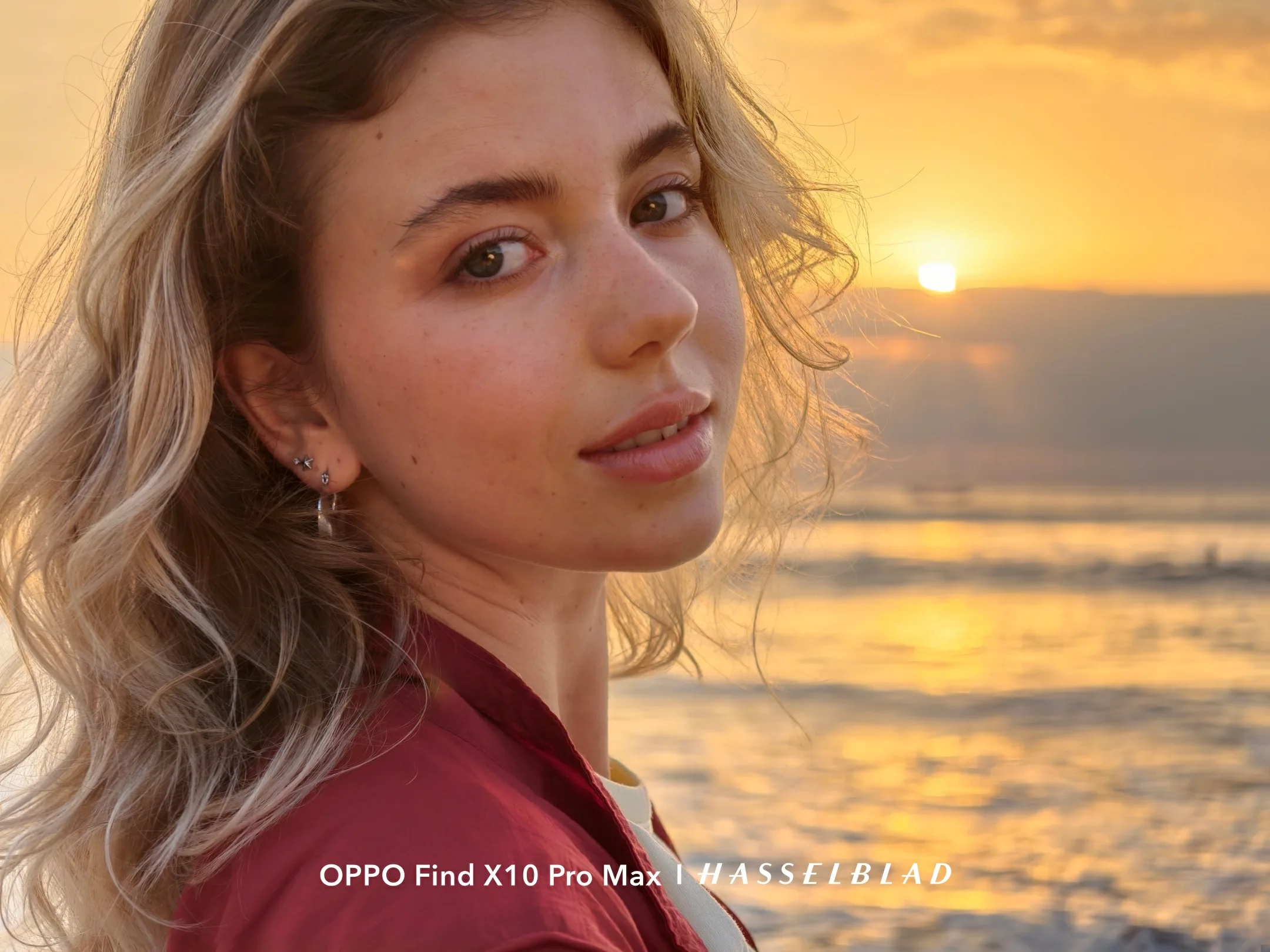 A woman with windswept blonde hair posing by the sea at sunset, shot on the Find X10 Pro Max