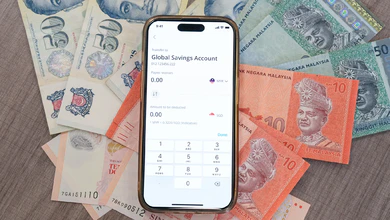 A smartphone showing an OCBC Global Savings Account transfer screen lies on Singapore dollar and Malaysian ringgit banknotes