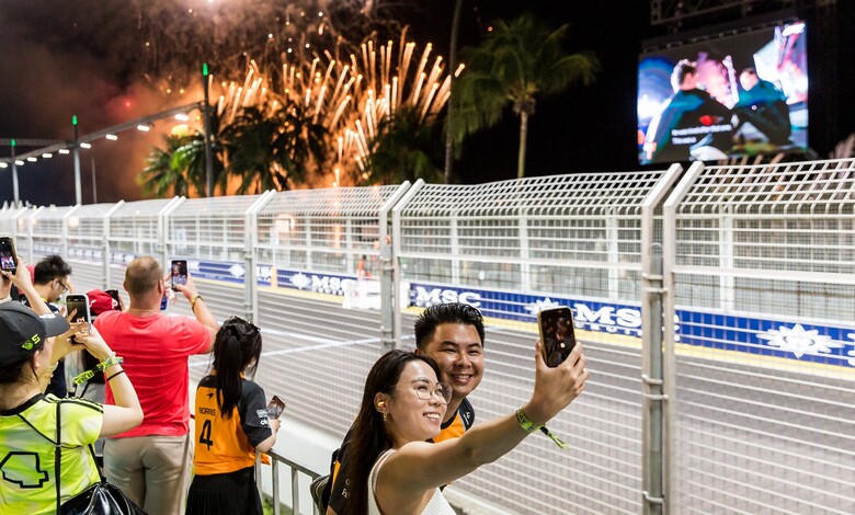 Fans take selfies at the circuit fence in front of the Zone 1 Skyline Grandstand, with fireworks above the Marina Bay Street