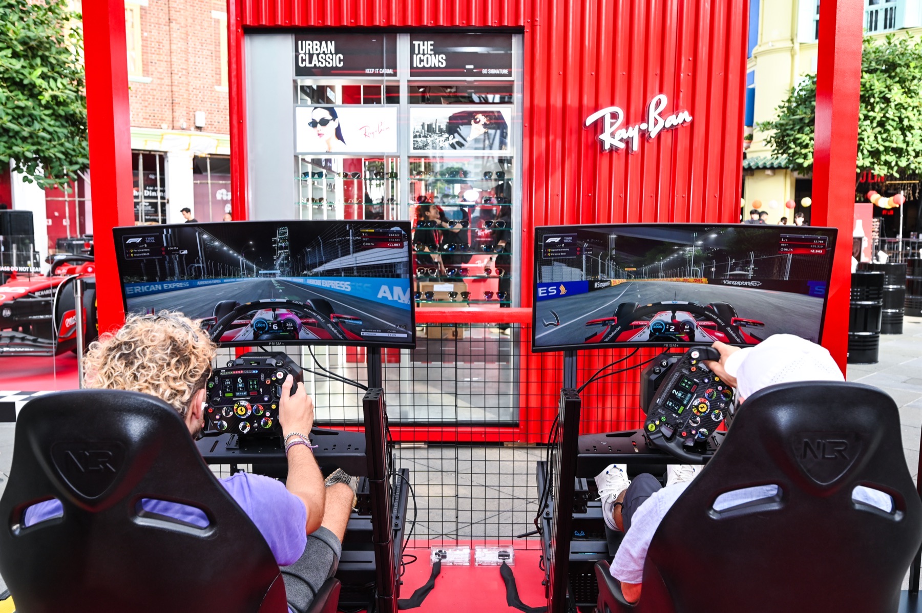 Two racing simulators side by side in front of the red Ray-Ban pop-up structure.