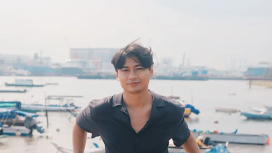 Firdaus Sani in a dark shirt standing in front of a harbour with moored boats and port cranes