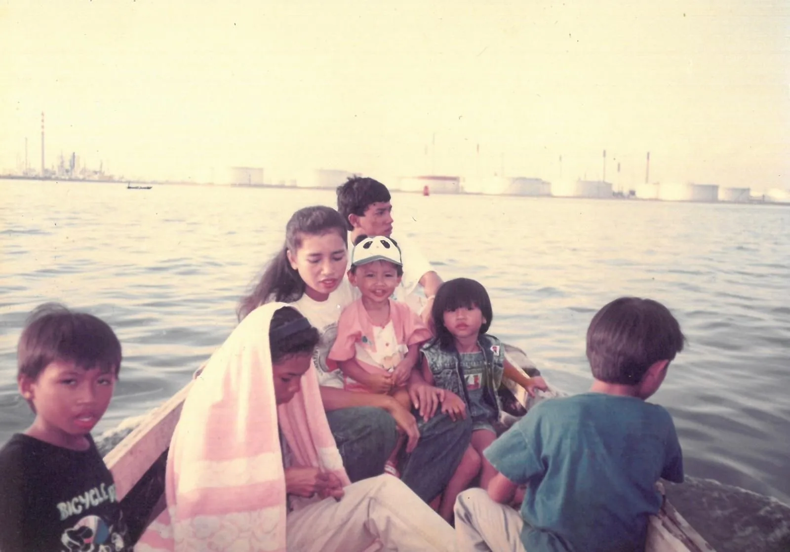 Firdaus Sani and his family on a small boat heading towards Pulau Semakau, with industrial tanks across the water