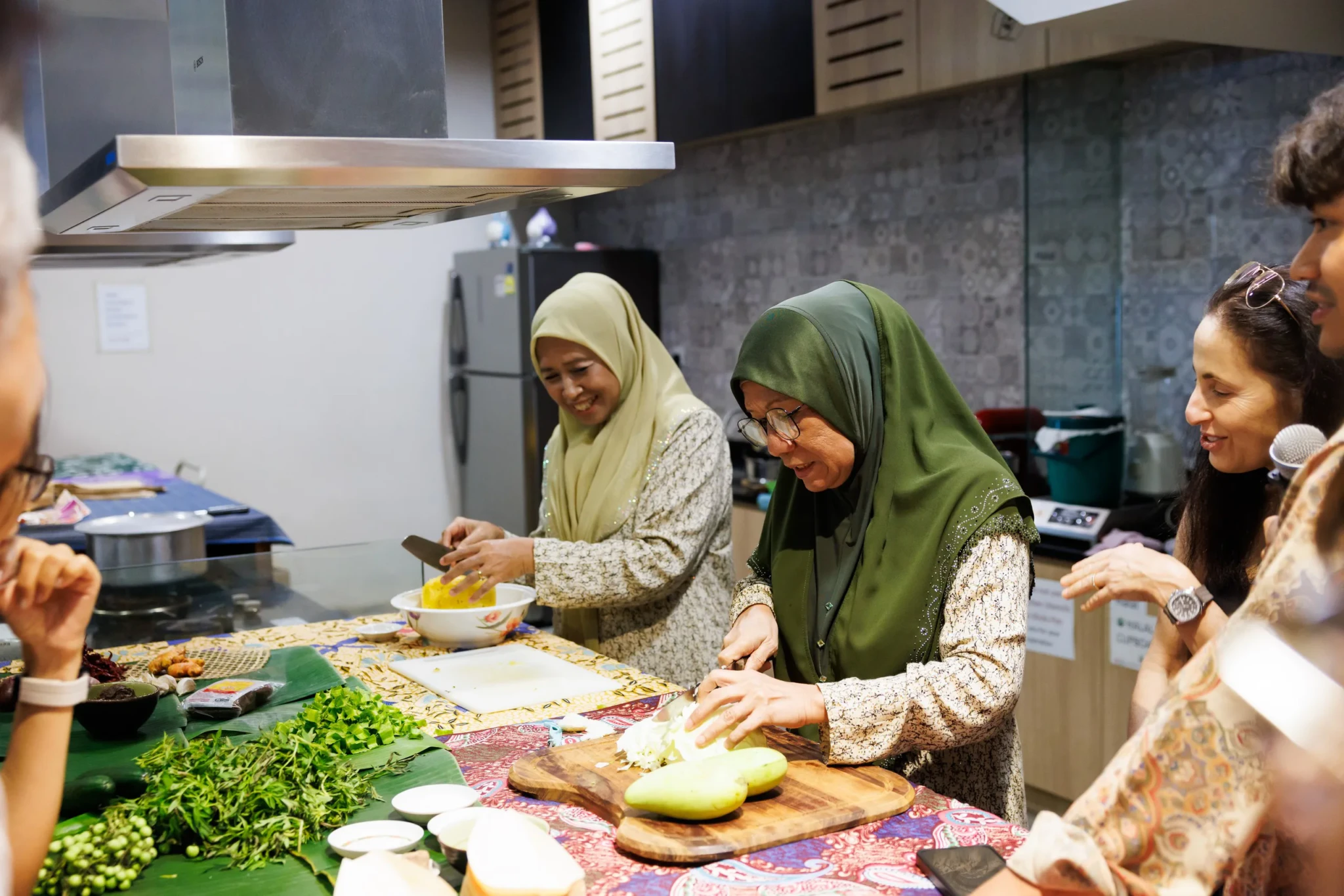 Mdm Noorani and Mdm Rohaini cooking Orang Pulau dishes at a counter while participants watch