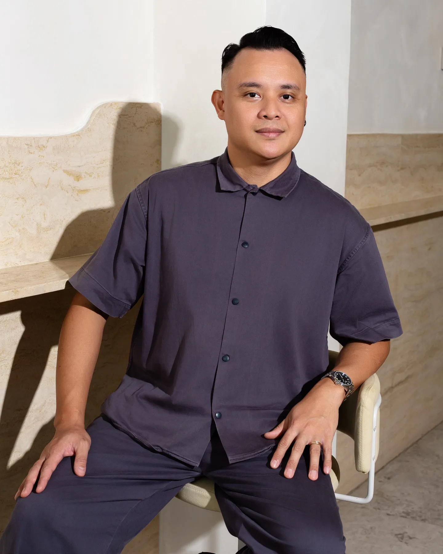 Bar Manager Mel Chavez seated in a cream chair against a travertine-lined wall
